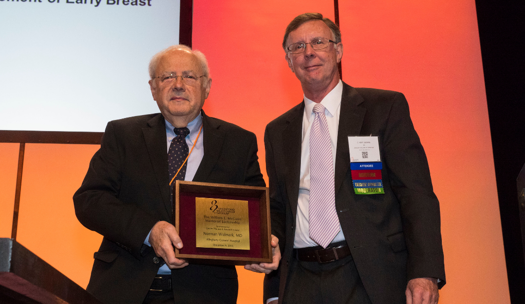 dr. norman wolmark holds his william mcguire award on a stage at sabcs 
